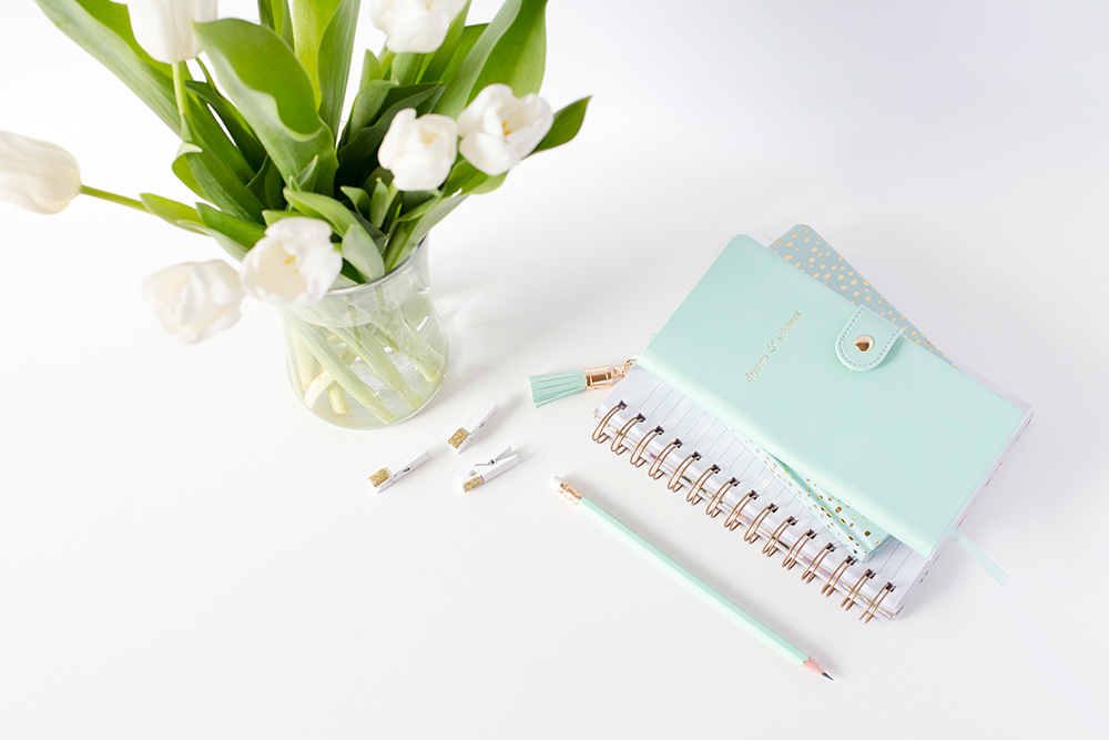Mint green notebook with pencil, paper clips, and vase of white tulips.