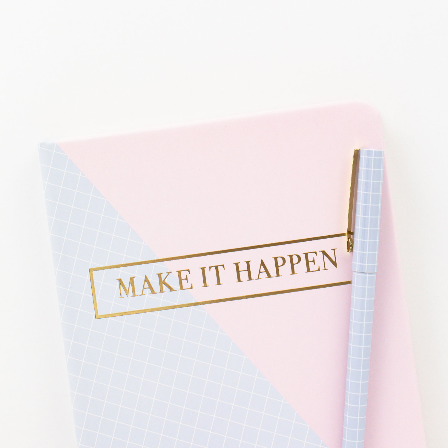 Pink and blue notebook with the words "Make it Happen" written on it and a blue dotted pen on top of it.